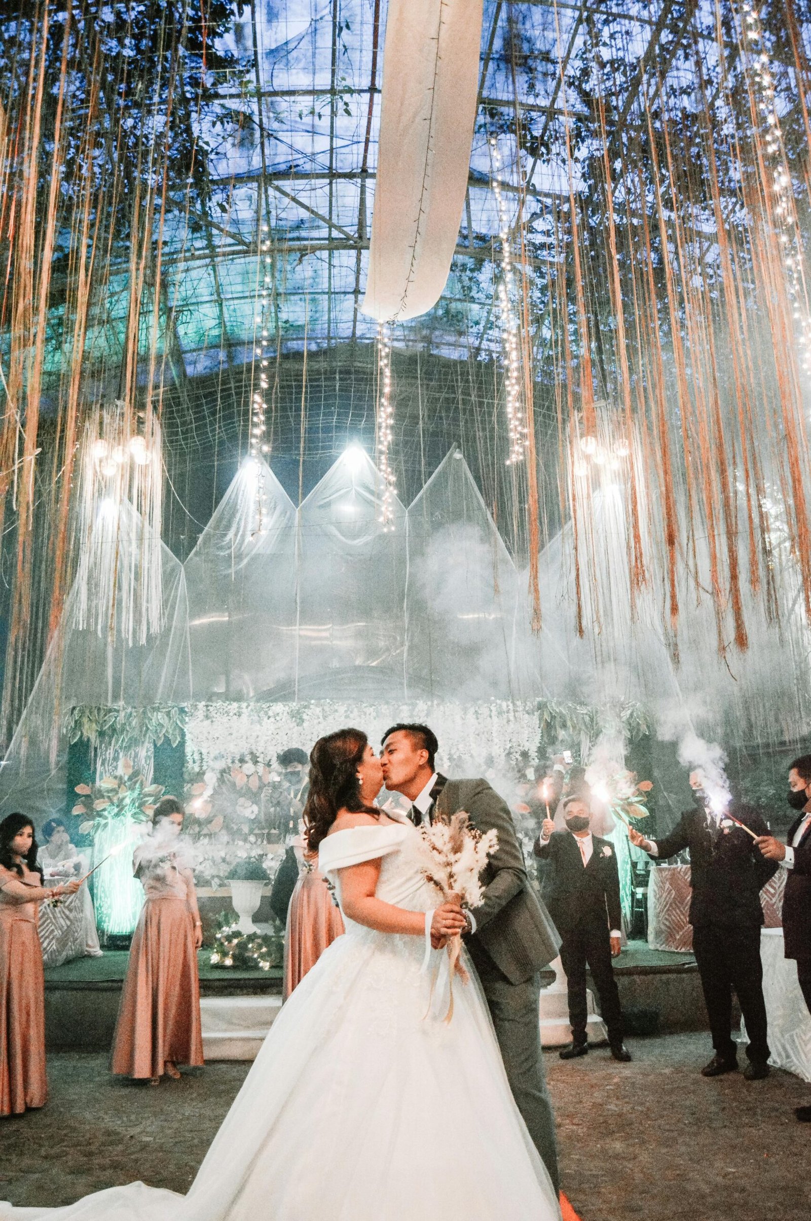 A newlywed couple shares a romantic kiss amidst a magical indoor wedding setup with sparklers.